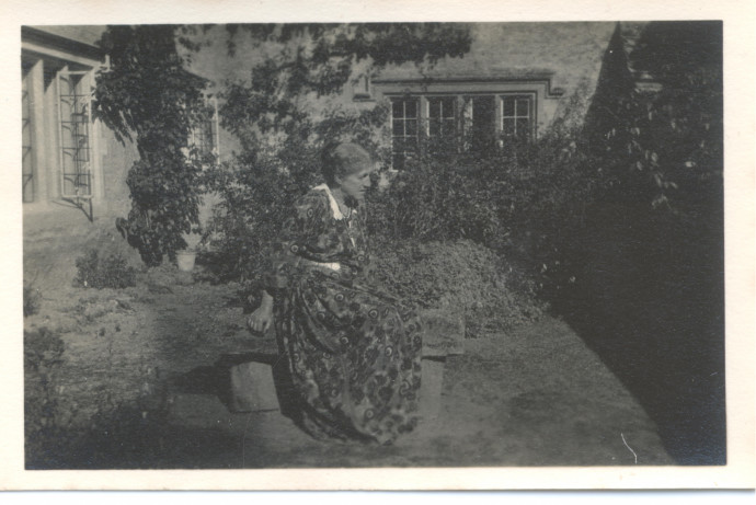 May Morris sits on a stone bench in a patterned dress.